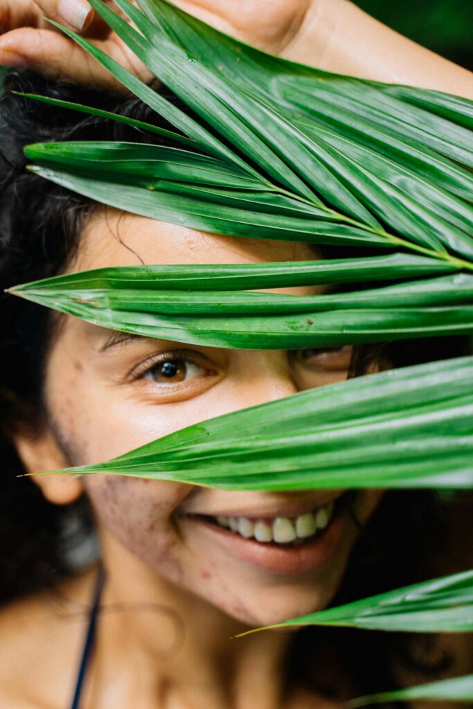 Portrait of a smiling woman partially obscured by lush green leaves.