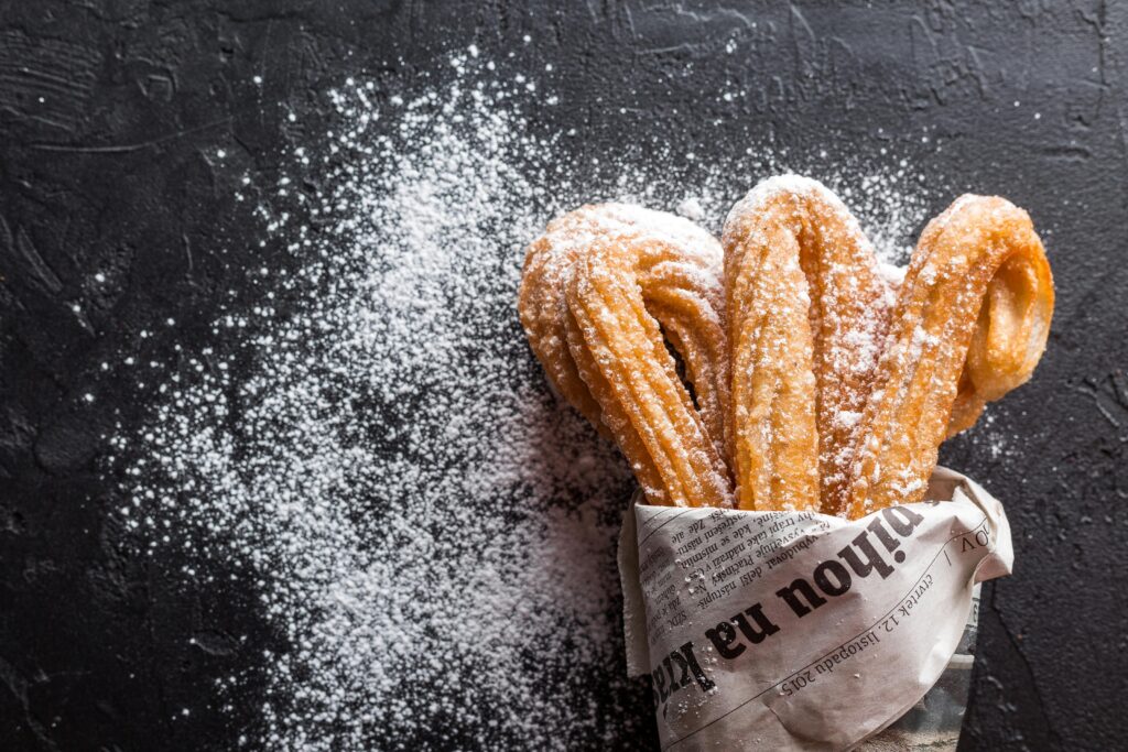 Close-up of freshly baked churros with powdered sugar on newspaper. A tasty dessert treat.